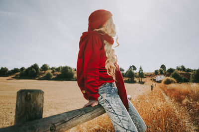 Woman sitting on railing in field against sky