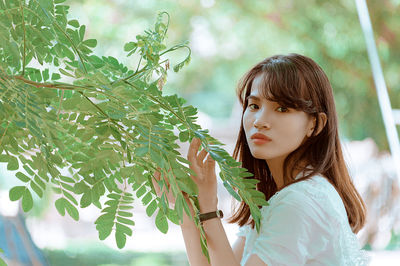 Side view portrait of young woman holding branches at park