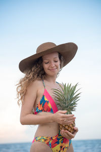 Woman holding pineapple while standing against sky