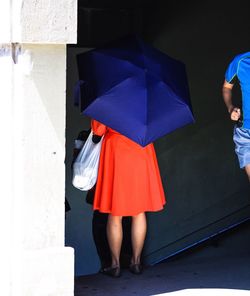 Rear view of woman with blue umbrella by building