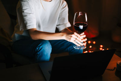 Young woman having video call on laptop computer and drinking wine.