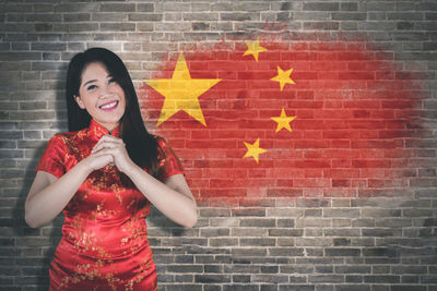 Portrait of a smiling young woman standing against brick wall