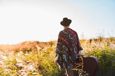 Man with acoustic guitar wearing poncho in a rural area at sunset