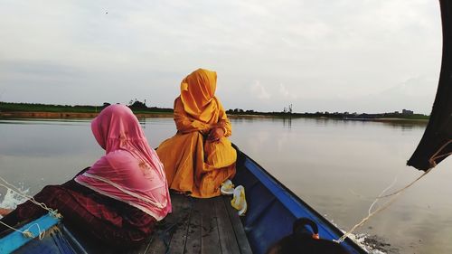 Rear view of people on boat in lake against sky