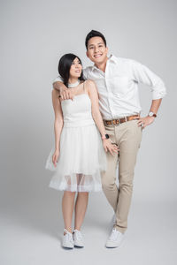 Full length portrait of smiling couple standing over gray background