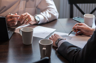 Midsection of business people working with coffee cups on desk at office