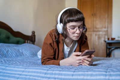 Relaxed music lover teenage girl listening to favourite single in headphones lying in bed at home.