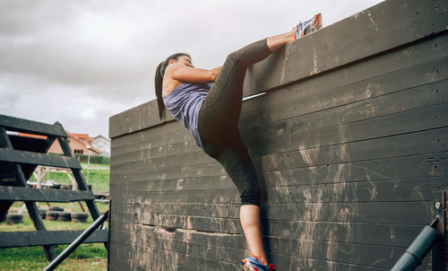 Woman climbing on wooden wall while exercising outdoors