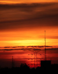 Silhouette electricity pylon against dramatic sky during sunset