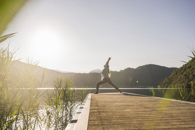 Woman stretching hands on jetty by lake and mountains at vacation