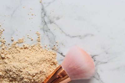 Directly above shot of make-up powder with brush over white marble