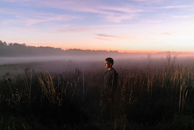Man standing on field against sky during sunset