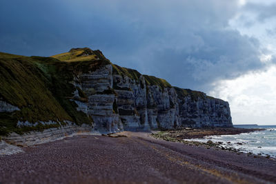 Scenic view of sea by mountain against sky