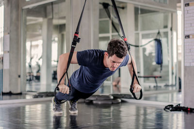 Man doing exercise with fitness straps to strengthen his abdominal muscle in gym.