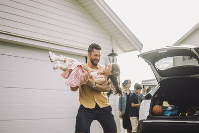 Happy father playing with daughter by electric car outside house