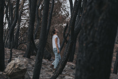 Woman walking amidst burnt trees in forest