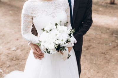 Midsection of bride and bridegroom standing outdoors