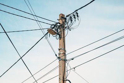 Street light with electricity utility pole and messy electrical wires against sky, low angle view