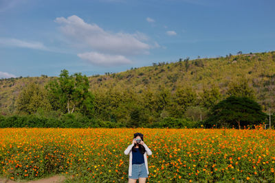 Woman photographing while standing on flower field against sky