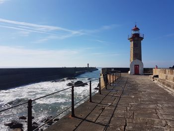 Lighthouse amidst buildings and sea against sky