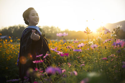 Side view portrait of woman smiling while standing amidst flowers during sunset