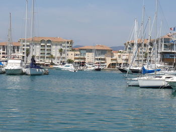 Boats moored at harbor by houses against sky