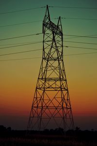 Low angle view of electricity pylon against sky at sunset