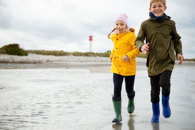 Full length of girl running with brother at beach