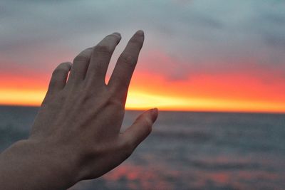 Cropped image of person gesturing against sea during sunset