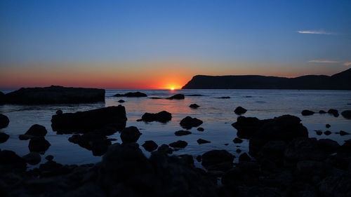 Scenic view of rocks on beach against sky during sunset