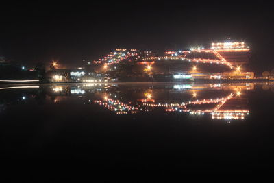 Illuminated city by river against sky at night