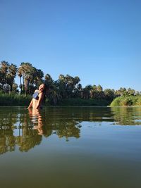 Rear view of woman swimming in lake against clear blue sky