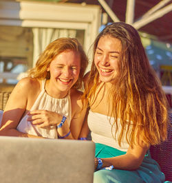 Happy female friends with laptop on sunny day