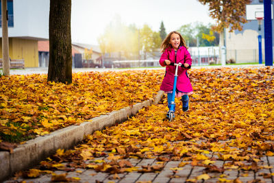 Portrait of girl riding push scooter at park during autumn