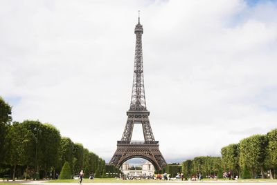 People in park by eiffel tower against cloudy sky