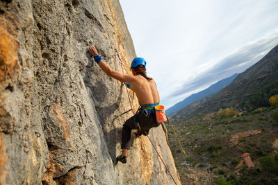 Shirtless man rock climbing against sky