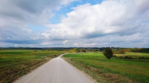 Empty road amidst grassy field against cloudy sky