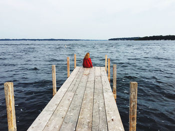 Rear view of woman sitting on pier by sea