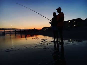 Silhouette people fishing at beach against clear sky