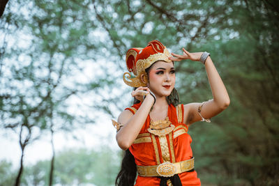 Portrait of young woman standing against trees