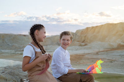 Teenage children talk and laugh while sitting at sunset near the river.