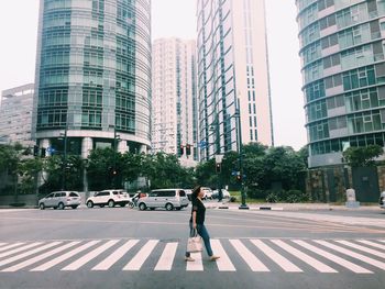 Woman crossing road against modern buildings