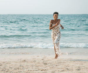 Portrait of happy woman running at beach against sky