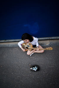 High angle view of young woman playing guitar by wall on street