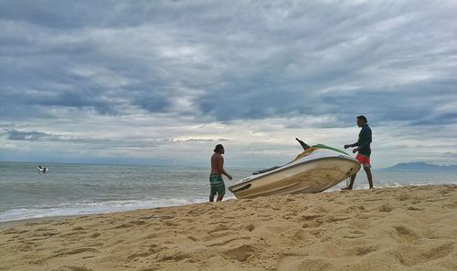 Men standing on beach against cloudy sky