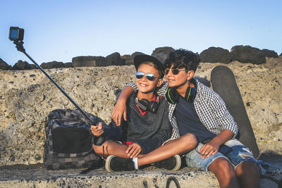 Brothers using mobile phone while sitting at beach