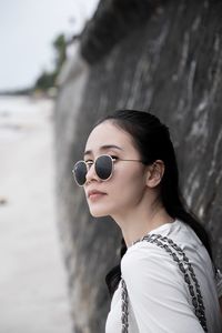 Young woman wearing sunglasses while standing by stone wall at beach