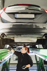 Mechanic examining car with hammer in auto repair shop