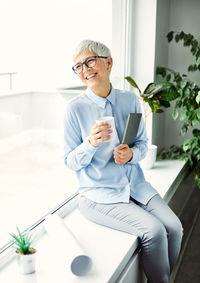 Smiling businesswoman with cup sitting near window