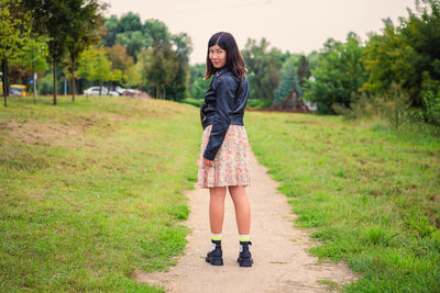 A young dark-haired girl stands on a footpath in the park and looks over her shoulder